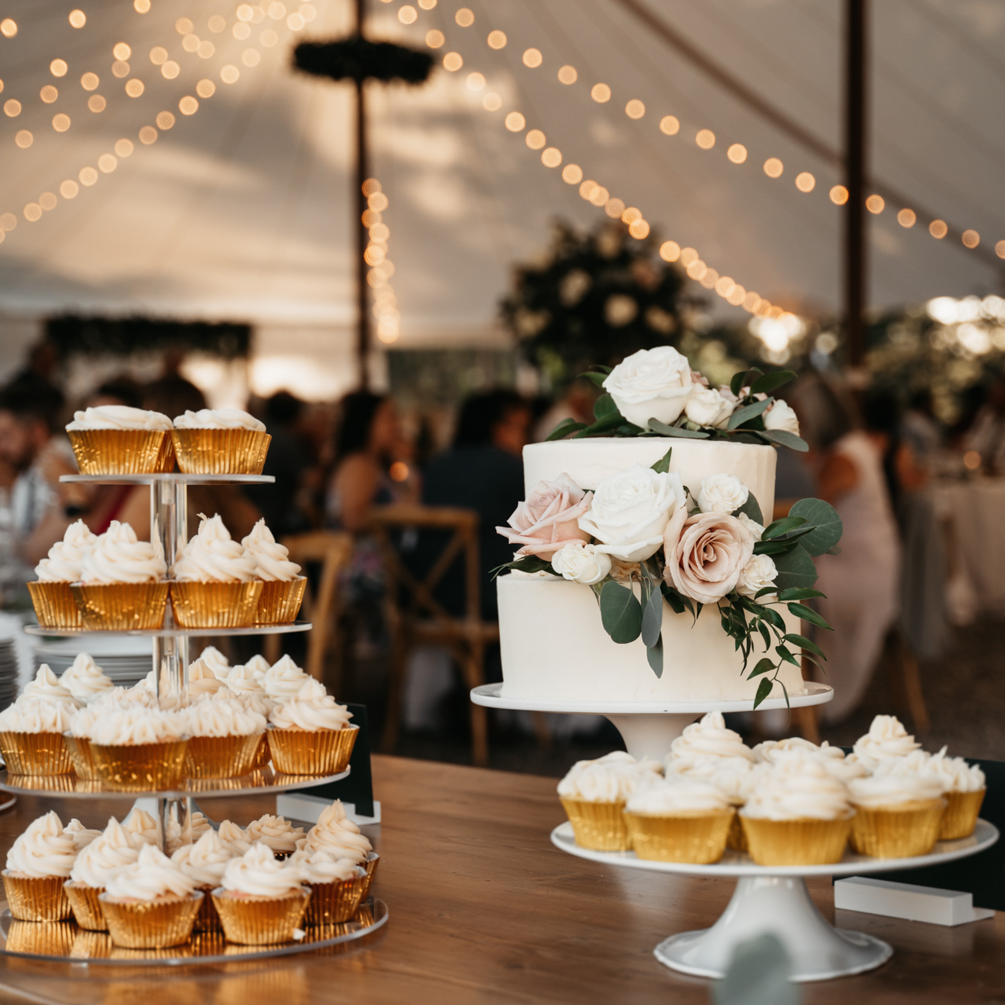 A display of cupcakes and wedding cake in a tent for a wedding reception