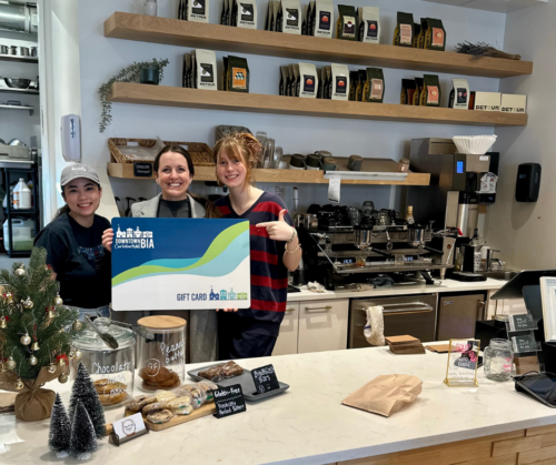 The Staff at Foundry and Owner Kaitey hold up a GIANT version of the Downtown Carleton Place Gift Card from behind the counter at Foudry Coffee Bar