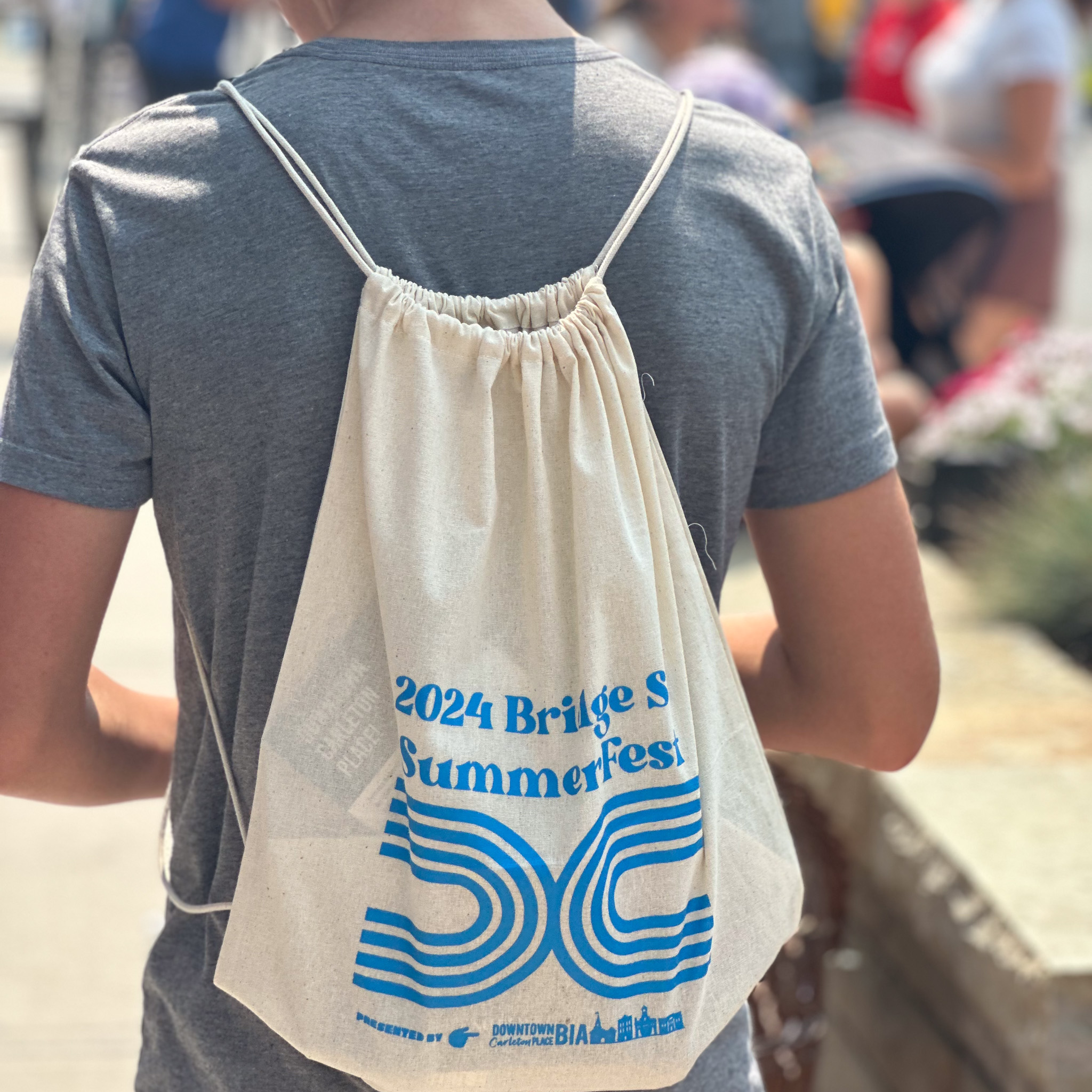 Child standing wearing the summerfest Swag bag in front of crowds
