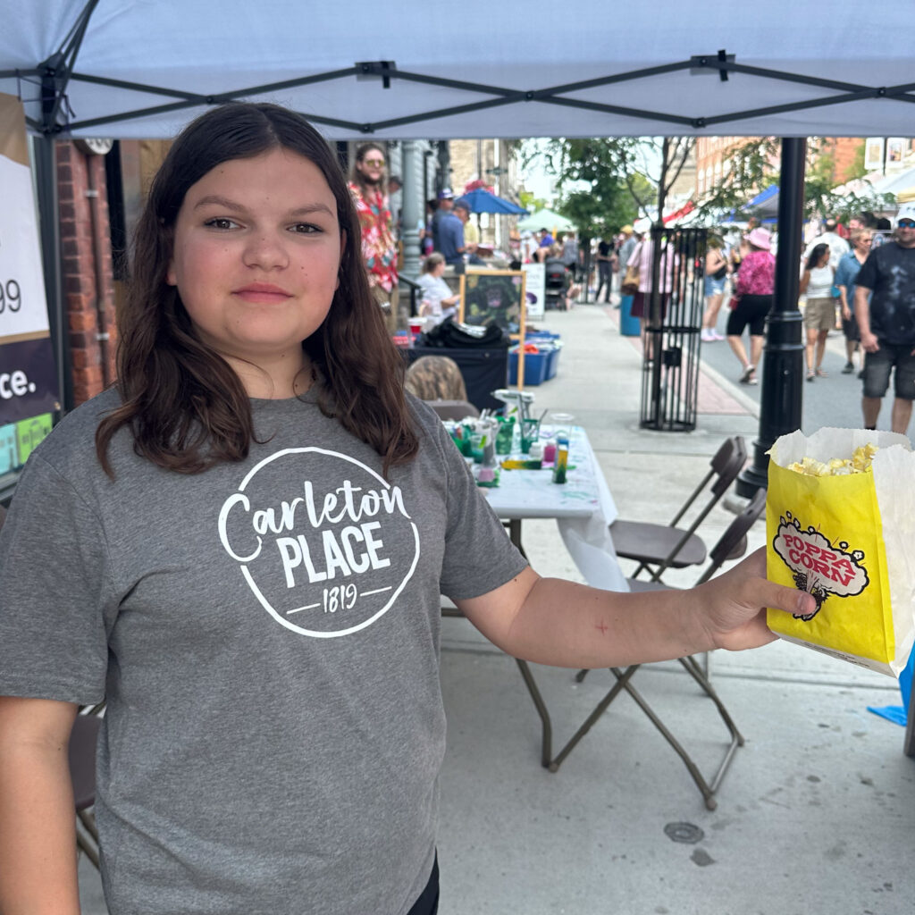 A girl wearing a Carleton Place Shirt offer popcorn to attendees
