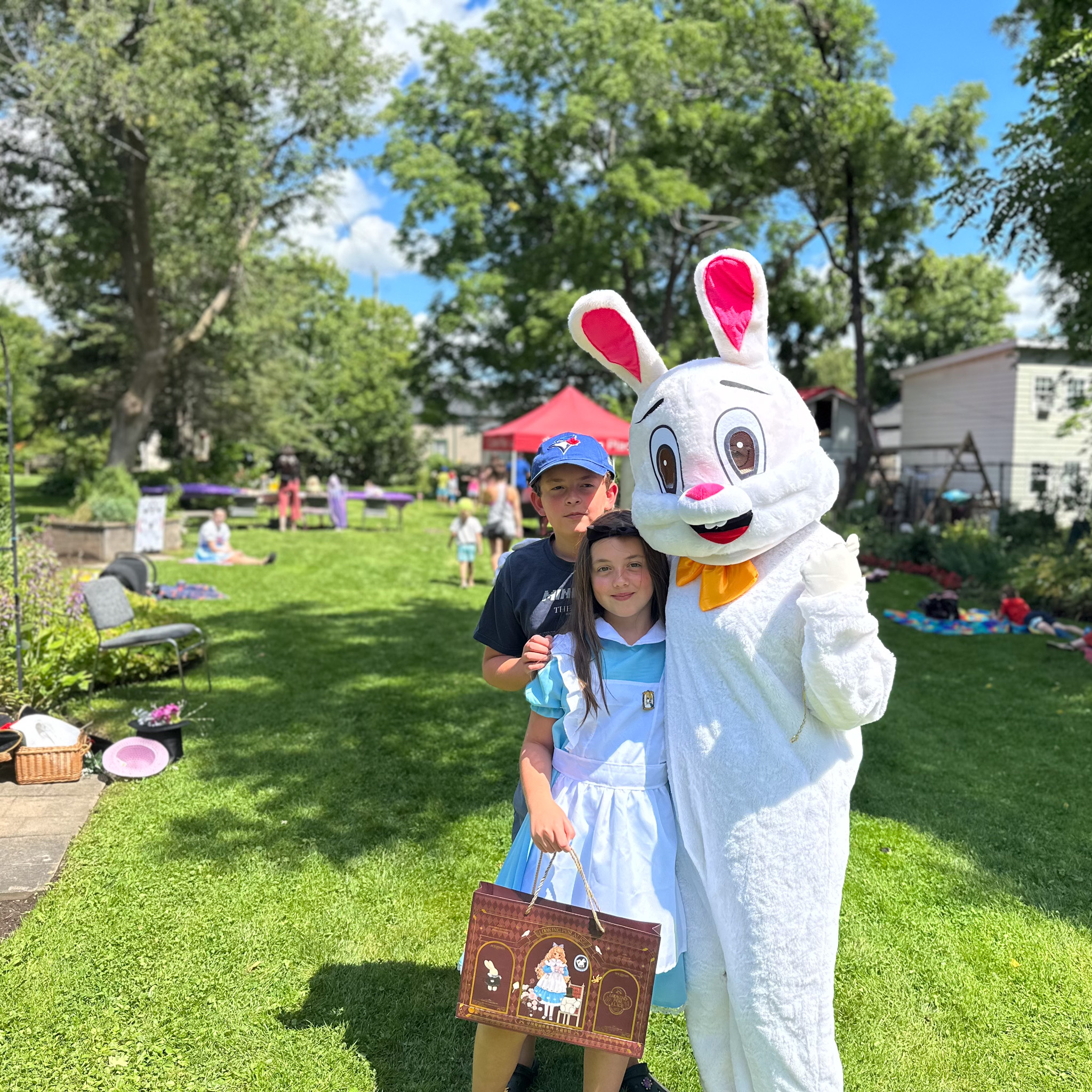 The white rabbit and alice gather for a photo with a young man in a garden