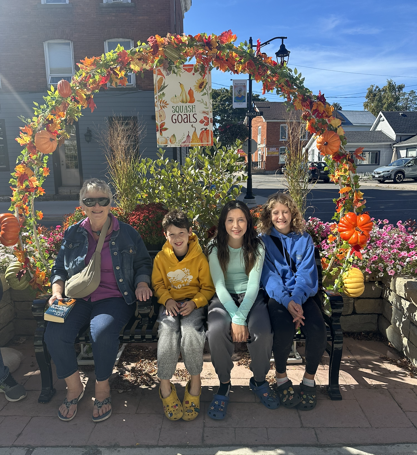 Pumpkinfest Downtown Family sitting under a fall themed arch. A sign reads "Squash Goals"